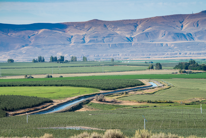 A canal flowing through a valley with agricultural fields around it.