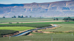 A canal flowing through a valley with agricultural fields around it.