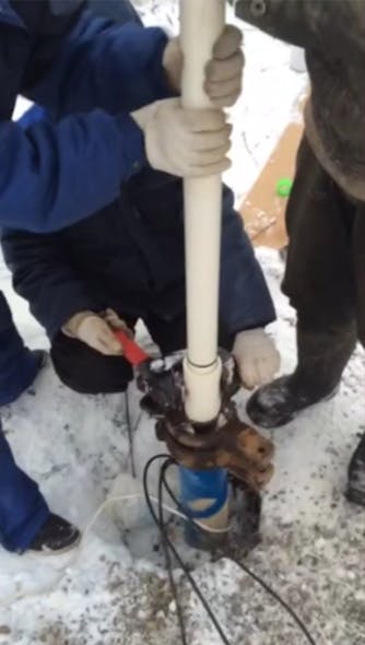 Workers install a uPVC pipe for a groundwater well in frozen ground.