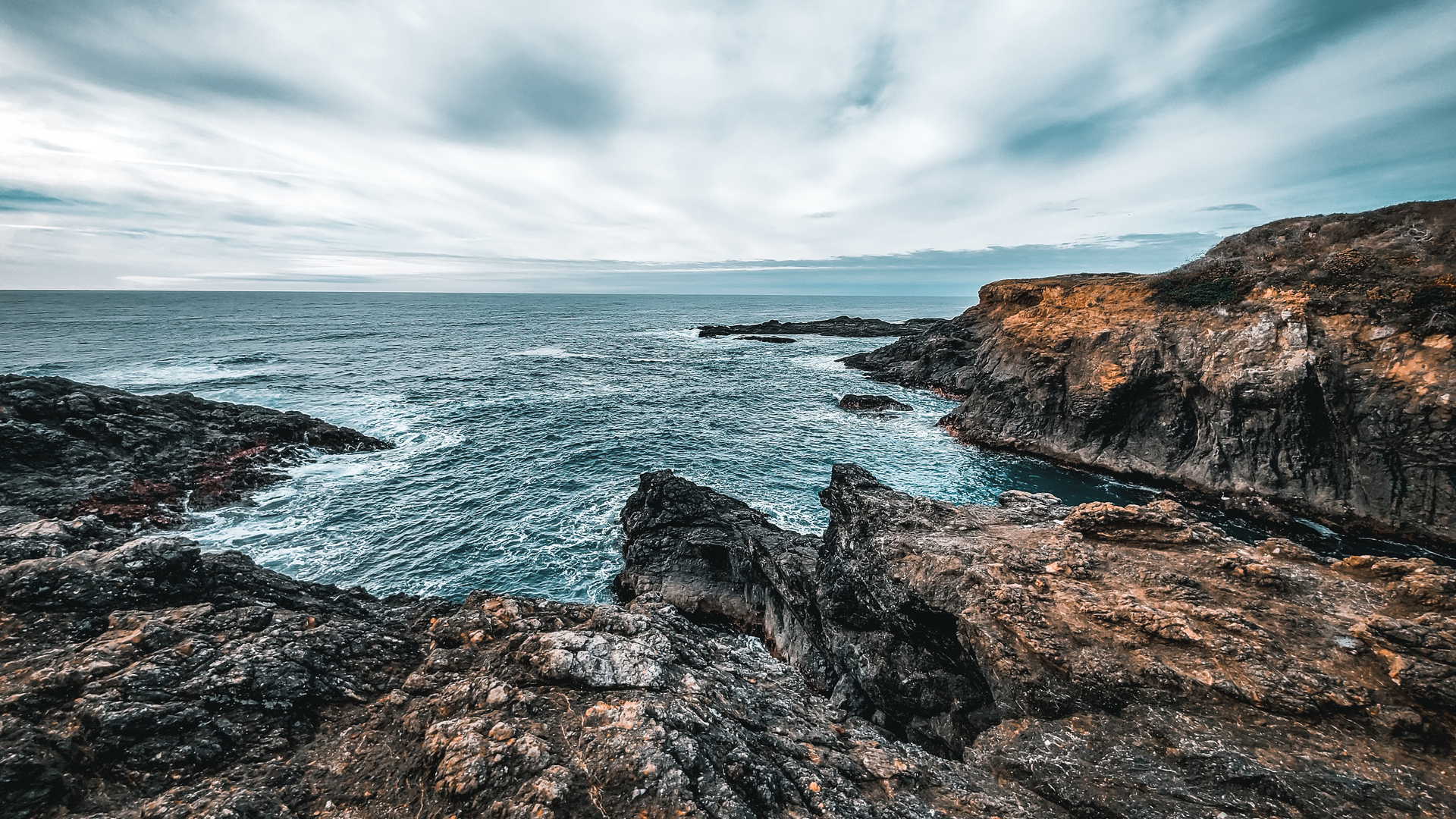 A view of the blue Pacific Ocean crashing into rocks at the glass beach in Fort Bragg, California.