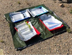 An experimental setup with Nalgene bottles, plastic water bottles, and a plastic bag placed on a reflective tarp exposed to the sunlight during a lower-altitude trial. An experimental setup with Nalgene bottles, plastic water bottles, and a plastic bag placed on a reflective tarp exposed to the sunlight during a lower-altitude trial.