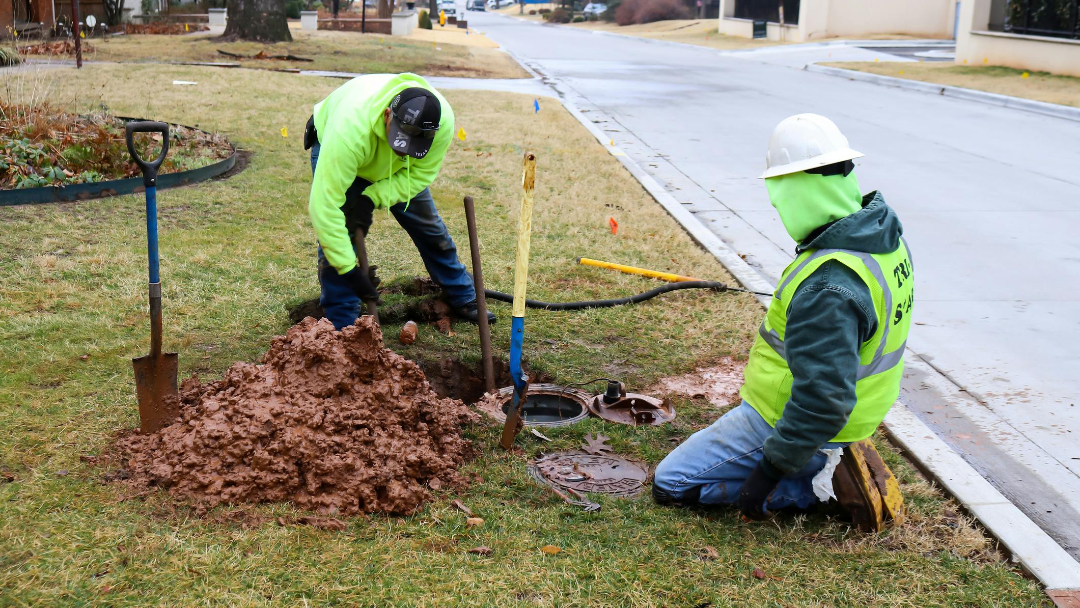 Two Workers fixing leak on water meter and digging out very wet mud on cold day in Tulsa Oklahoma USA