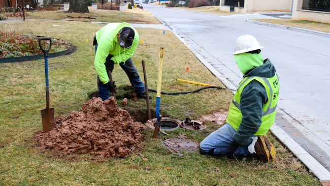 Two Workers fixing leak on water meter and digging out very wet mud on cold day in Tulsa Oklahoma USA