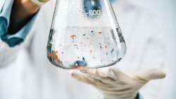 Person holding a laboratory beaker containing microplastics in liquid. Person holding a laboratory beaker containing microplastics in liquid.